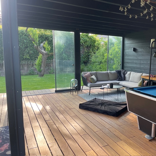 Ein modernes Gartenhaus mit Glasfront grenzt direkt an eine hochwertige Terrasse aus Ipe