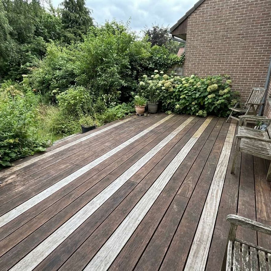 Eine moderne Terrasse aus Sucupira Terrassendielen neben einer Klinkerwand und einem grünen Garten