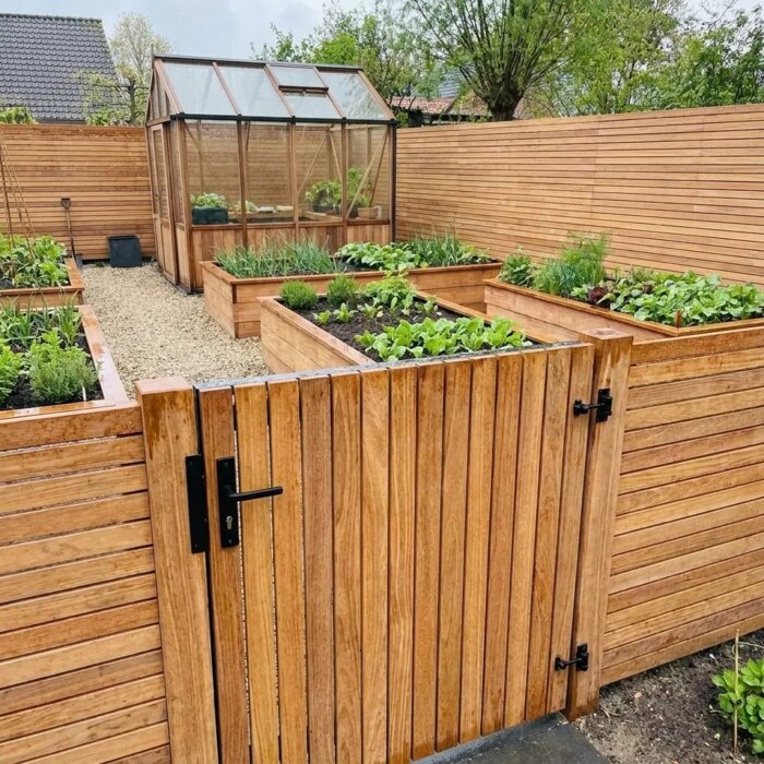 Teakholz Gartentor mit 7 cm Lamellen im Teak Zaun um einen Gemüsegarten mit Gewächshaus