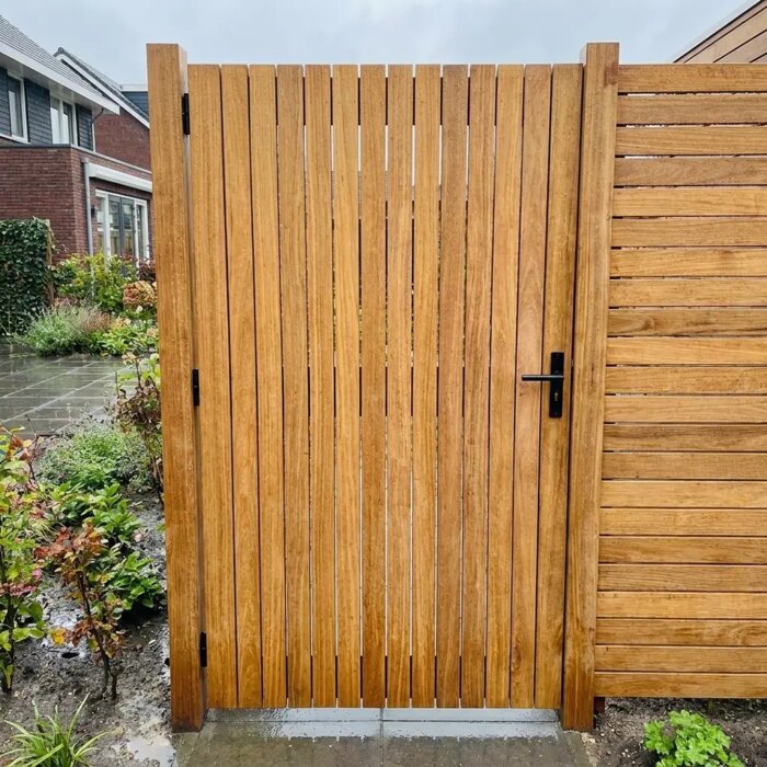 Teakholz Gartentor mit breiten 9 cm Lamellen nach einem Regenschauer, neben einem Teak Zaun