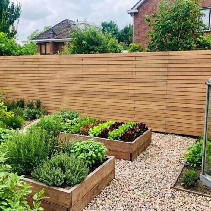 Um den Gemüsegarten: Teak Zaun mit 7 cm Lamellen hinter Hochbeeten und einem Gewächshaus