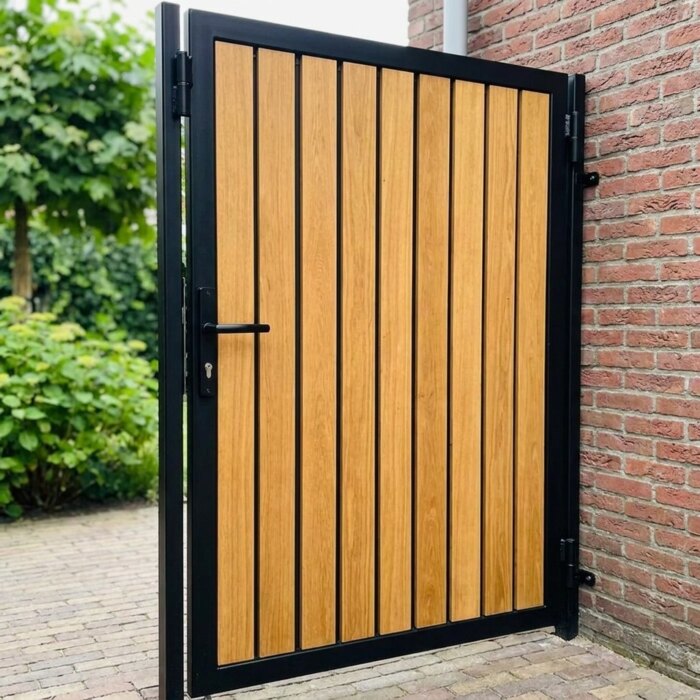 Schwarzer Stahlrahmen und Scharnier eines Teak Gartentors neben einem kräftigen Torpfosten
