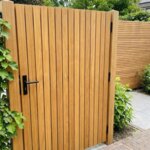 Gartentor aus Teakholz mit 5 cm Lamellen neben einer Kletterhortensie, mit schwarzem Türdrücker