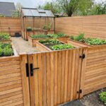 Teakholz Gartentor mit 7 cm Lamellen im Teak Zaun um einen Gemüsegarten mit Gewächshaus
