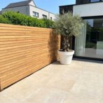Teak Zaun mit 7 cm Lamellen in einem Neubaugarten mit Olivenbaum