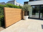 Teak Zaun mit 7 cm Lamellen in einem Neubaugarten mit Olivenbaum