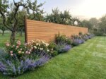 Teak Zaun mit 9 cm Lamellen in einem Landhausgarten mit Rosen und Obstbäumen